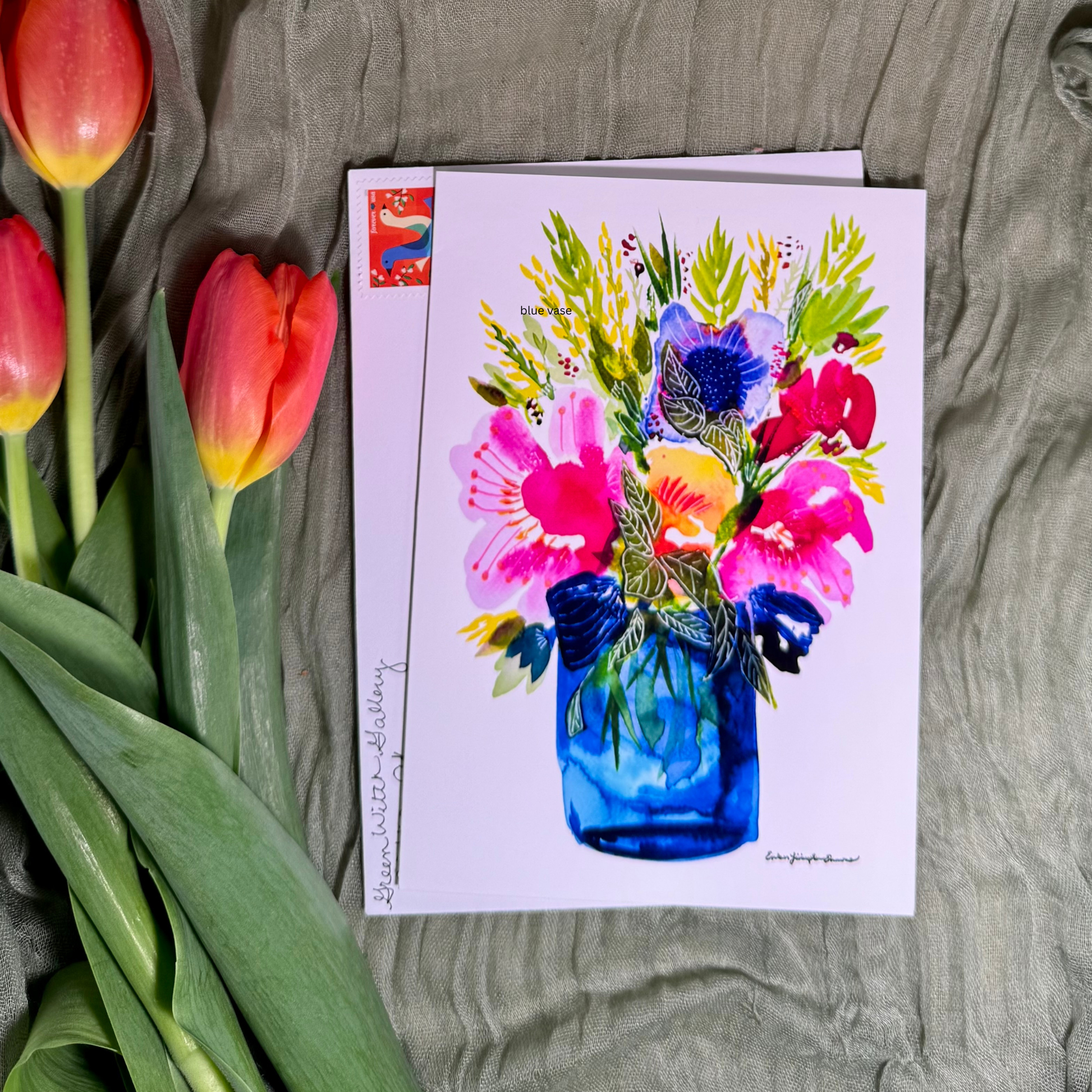 Greeting card with floral design next to red tulips on a textured surface