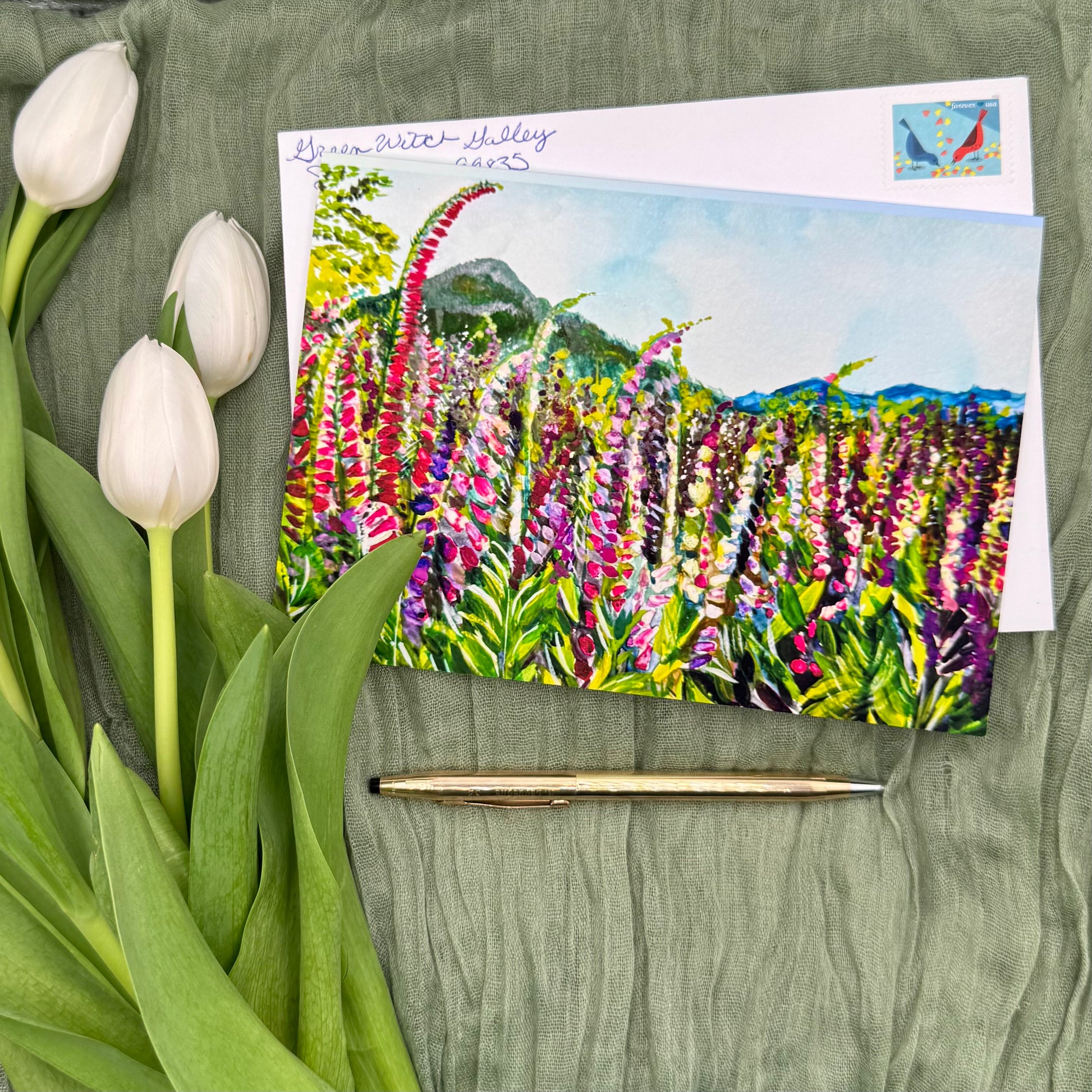 Greeting card with floral design, envelope, pen, and tulips on a green fabric background