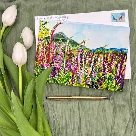 Greeting card with floral design, envelope, pen, and tulips on a green fabric background